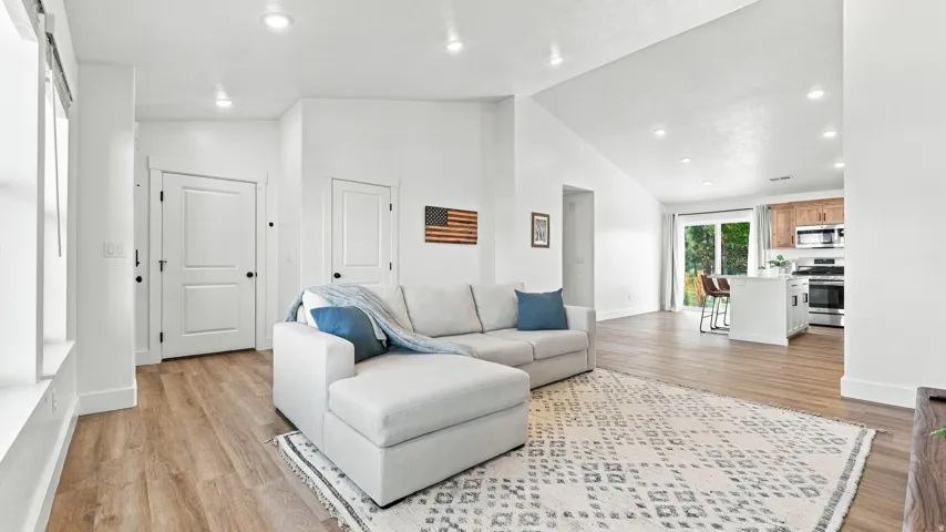 Vaulted ceiling with recessed lighting, wood-finish flooring, white shaker-style kitchen island, stainless steel range, and sliding glass door