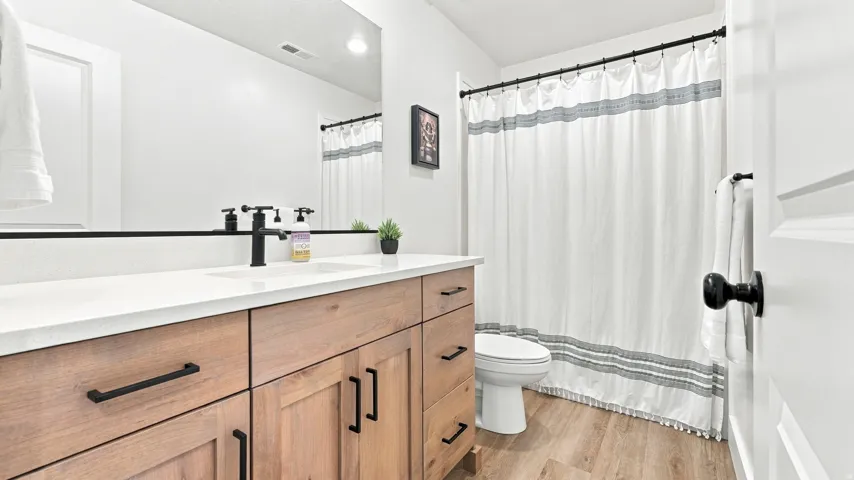 Bathroom featuring a wood-finish vanity with a light-toned countertop, matte black hardware, a toilet, and wood-finish flooring