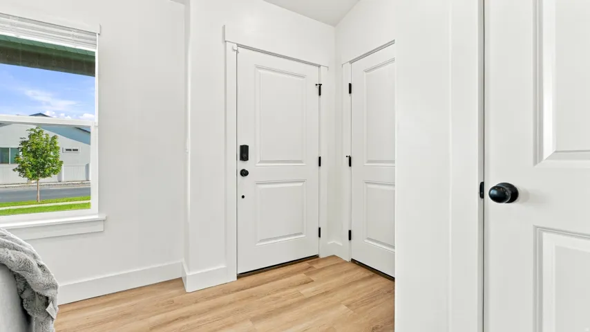 White interior doors, matte black hardware, wood-finish flooring, white window trim, and white walls