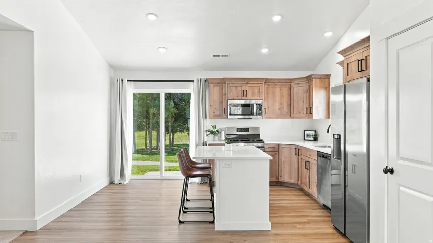 Kitchen featuring wood-finish cabinetry, stainless steel appliances, a center island with countertop seating, and wood-finish flooring