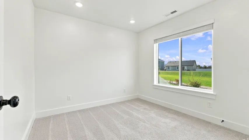 Recessed ceiling lighting, carpeted flooring, white walls, and a large window with roller shades