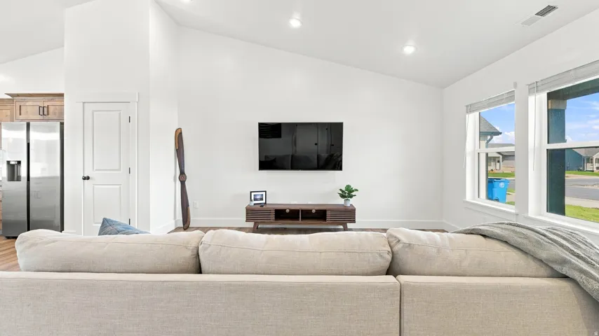 Vaulted ceiling, recessed lighting, wood-finish flooring, two large windows, and a built-in media console