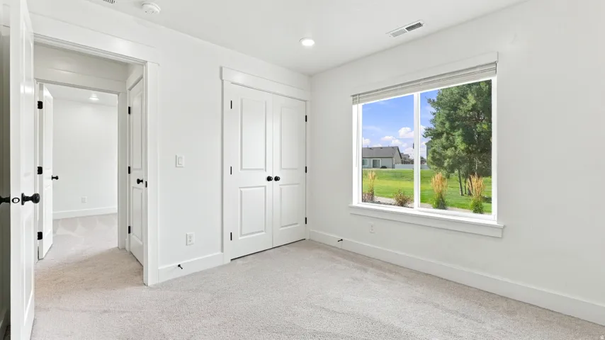 Neutral-toned carpet flooring, white walls, and a large window with white trim