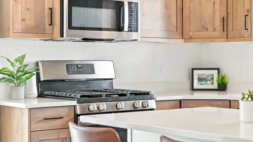 Stainless steel gas range, microwave, wood-finish cabinetry, and solid surface countertops