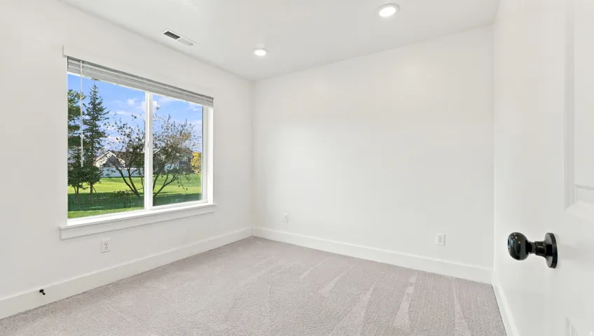 Recessed lighting, large window with surrounding trim, light-colored carpeting, white walls, and a black doorknob