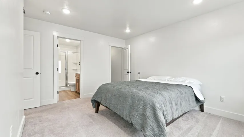 Recessed lighting, light-toned carpeting, white walls, and a wood-finish flooring visible through the doorway