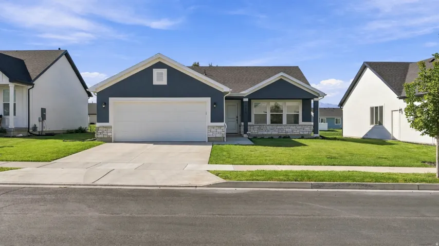 Single-story exterior with dark siding and stone accents, featuring an attached garage, a paved driveway, and a front lawn