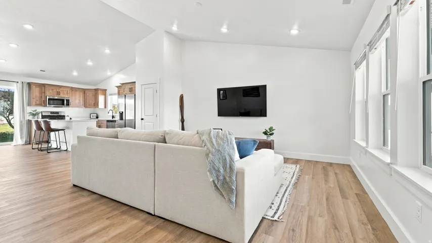 Vaulted ceilings, wood-finish flooring, white walls, multiple windows, and a kitchen featuring wood cabinetry