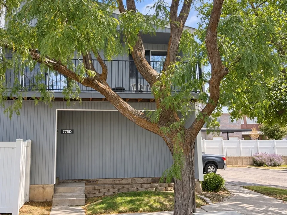 Two-story exterior with vertical siding, a second-floor balcony with metal railings, and a concrete pathway leading to the entry