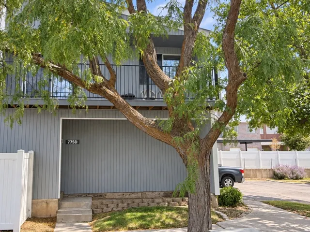 Two-story exterior with vertical siding, a second-floor balcony with metal railings, and a concrete pathway leading to the entry