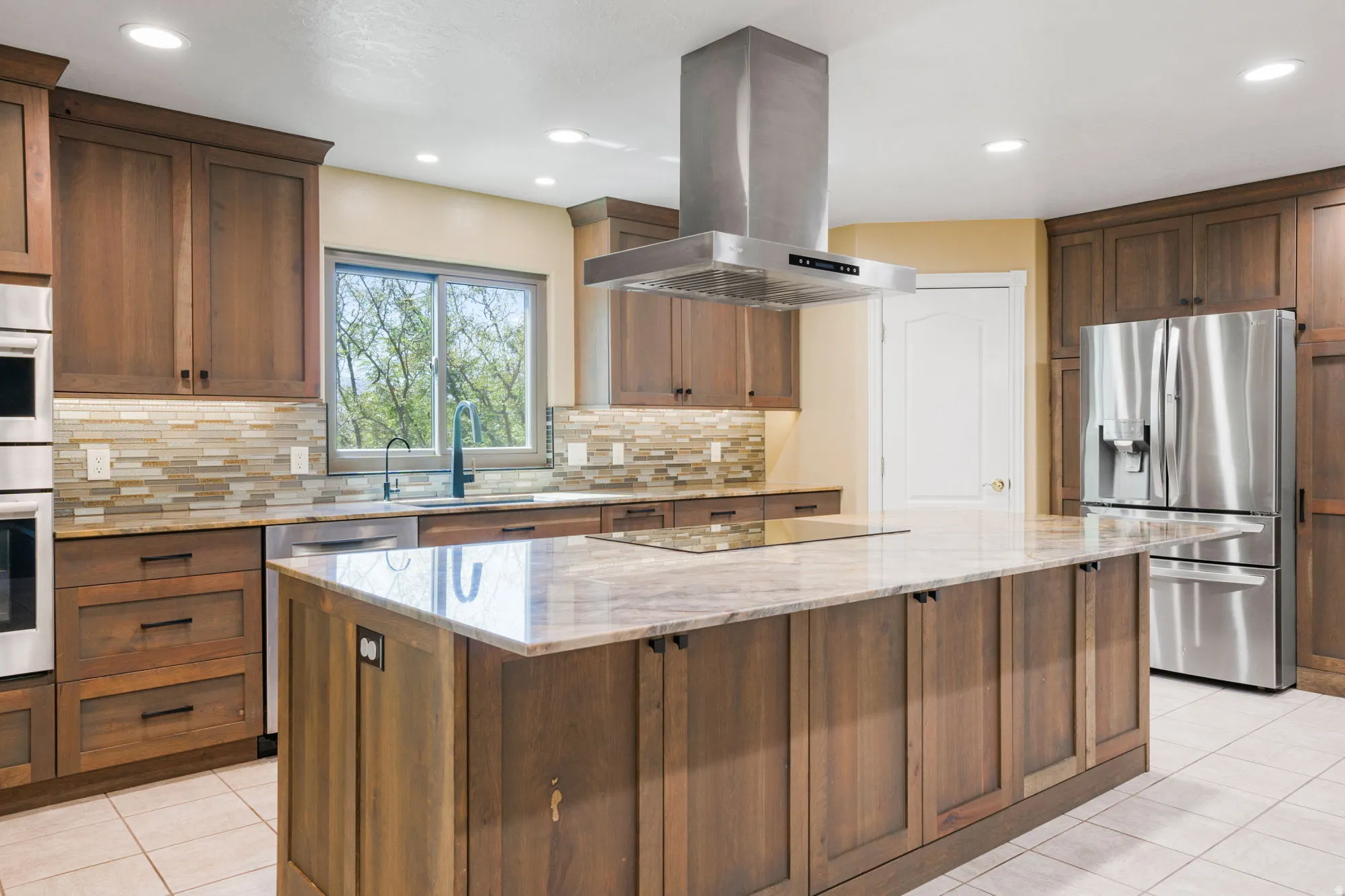 Full kitchen featuring wood cabinetry, stainless steel appliances, a center island with a built-in cooktop, and an overhead range hood