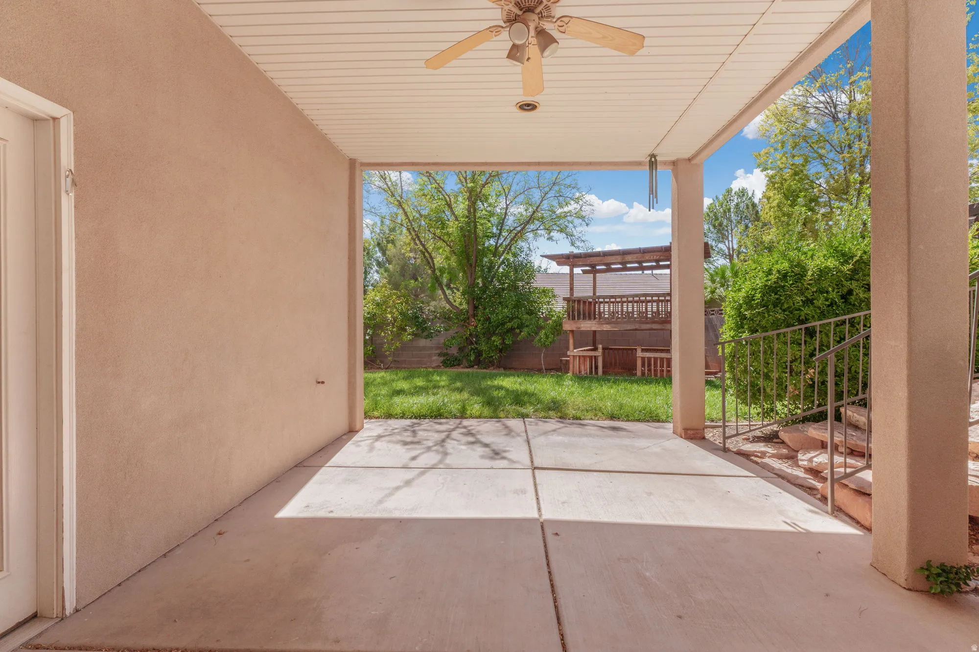 Covered patio with a ceiling fan, concrete flooring, and direct access to a fenced yard with a multi-level deck structure