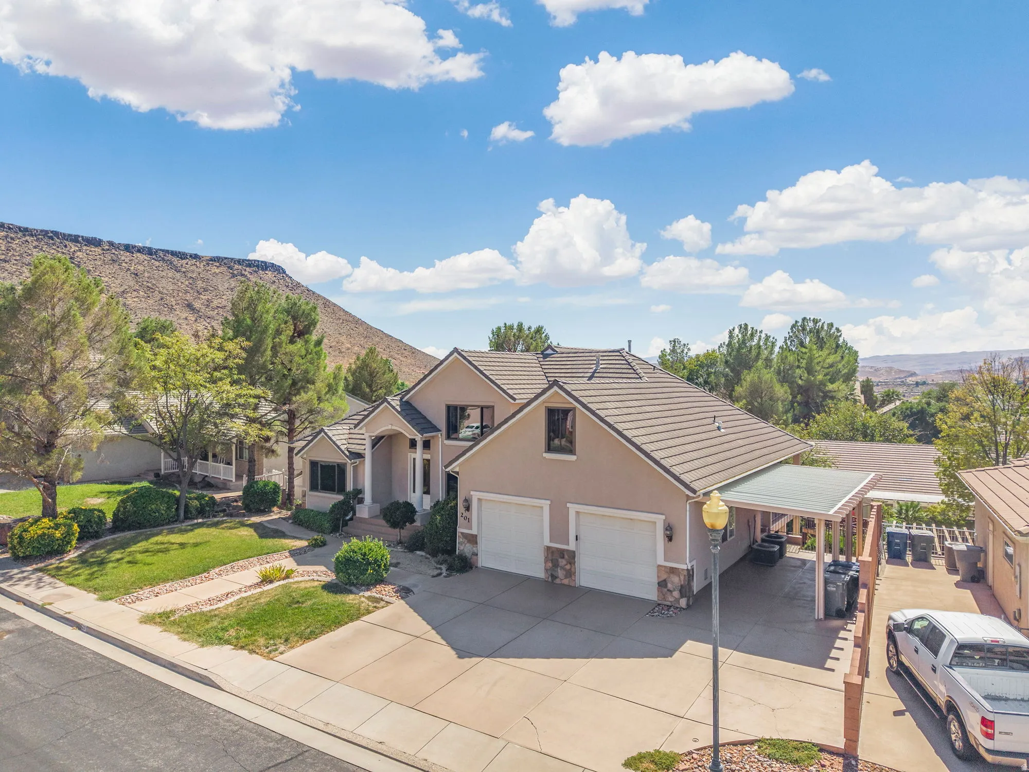 Stucco exterior with stone accents, two-car garage, covered carport, and a front lawn with mature trees