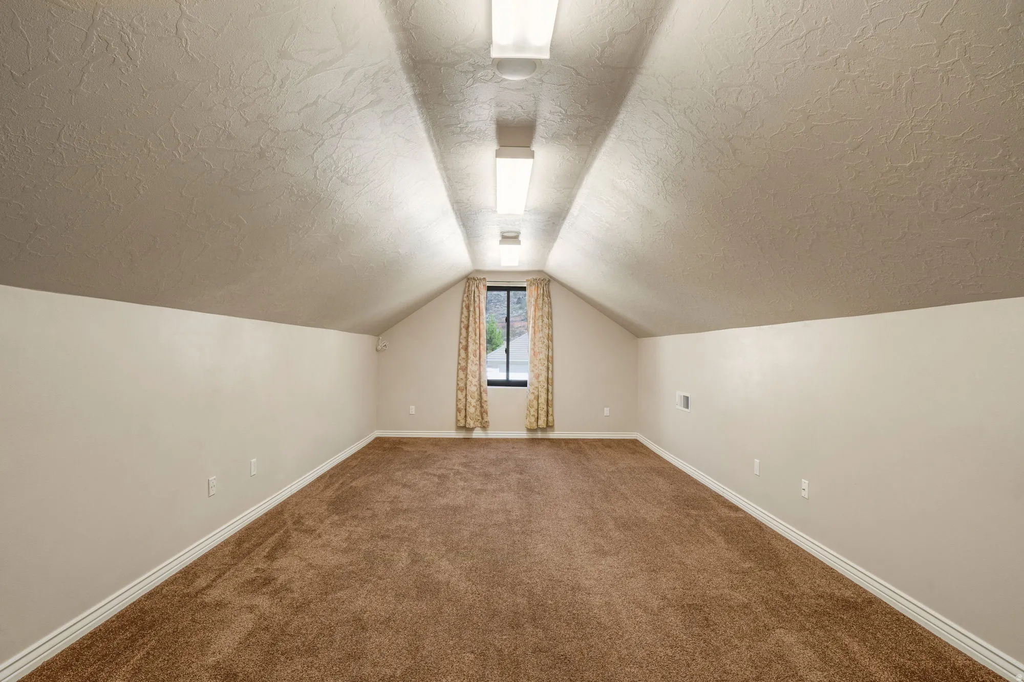 Spacious room with sloped ceilings, brown carpet, textured walls, and a recessed window