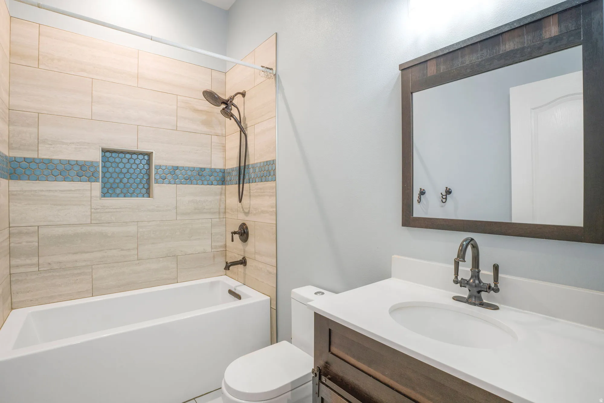 Built-in bathtub with a bronze shower fixture, tile surround with mosaic accent, and recessed shelf