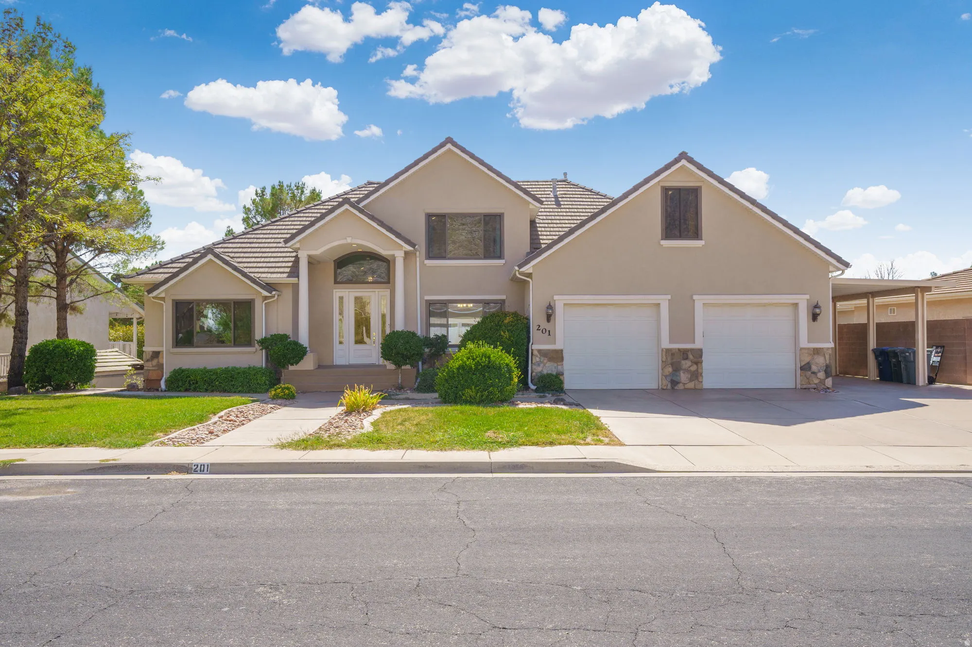 Stucco exterior with stone accents, two-car garage, covered carport, arched entry, and tiled roof