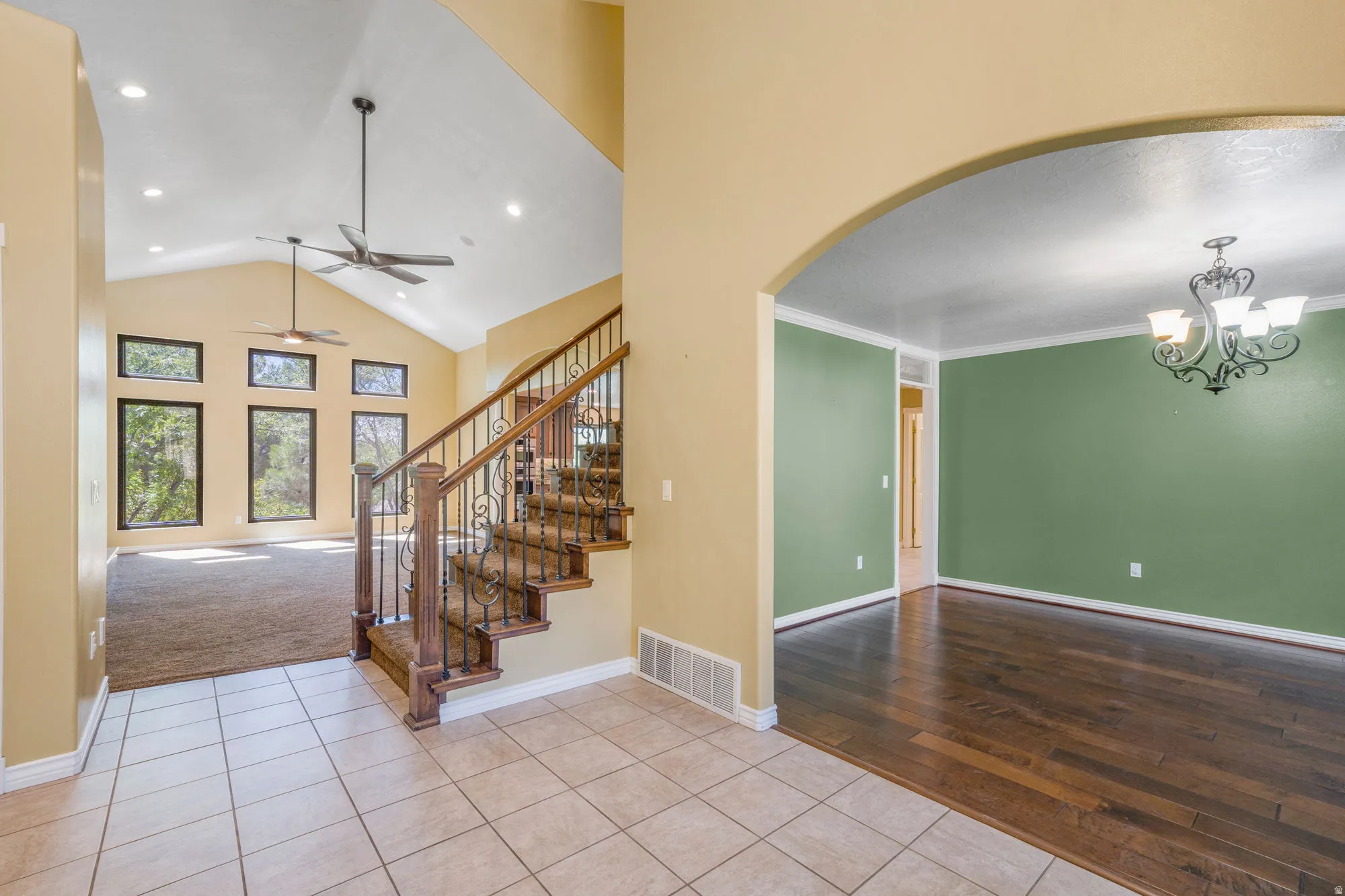 Vaulted ceiling with recessed lighting, tile entry flooring, wood-finish flooring, staircase with wrought iron balusters, and an arched doorway