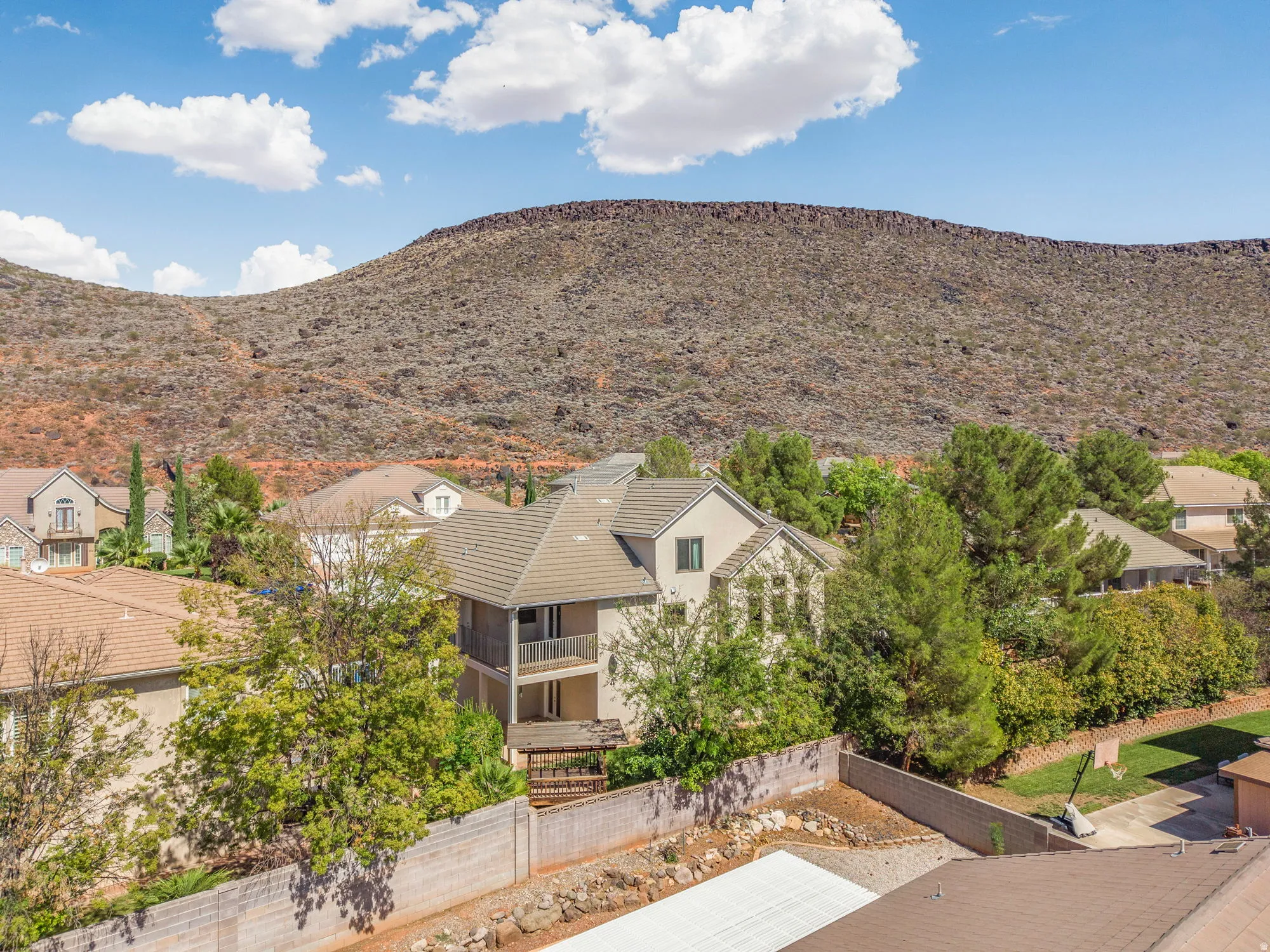 Tile roof residence with a stucco exterior, featuring a second-story balcony and a paved ground-level patio
