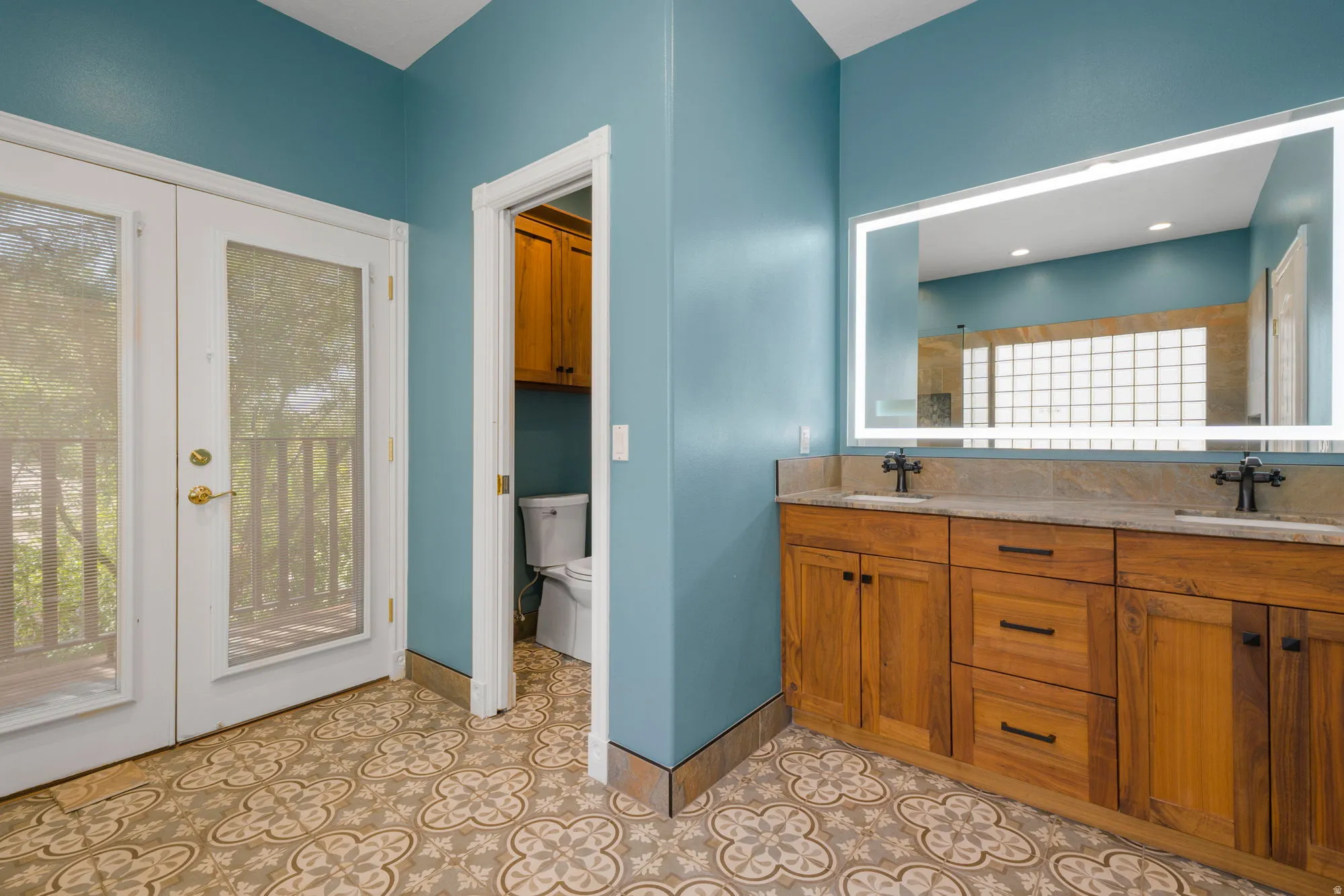 Dual wood-finish vanity with stone countertop, integrated sinks, and individual wall-mounted faucets