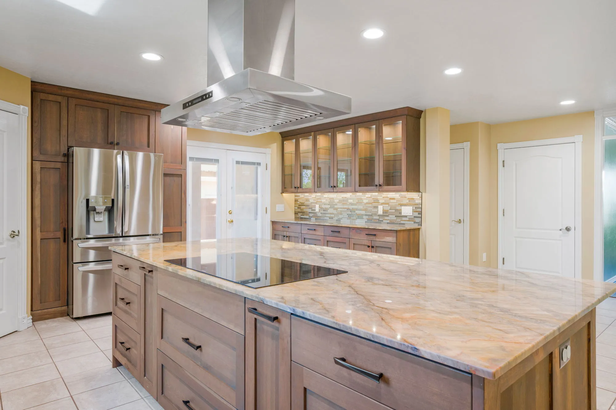 Spacious kitchen island with an integrated cooktop, stone countertop, stainless steel appliances, and extensive cabinetry