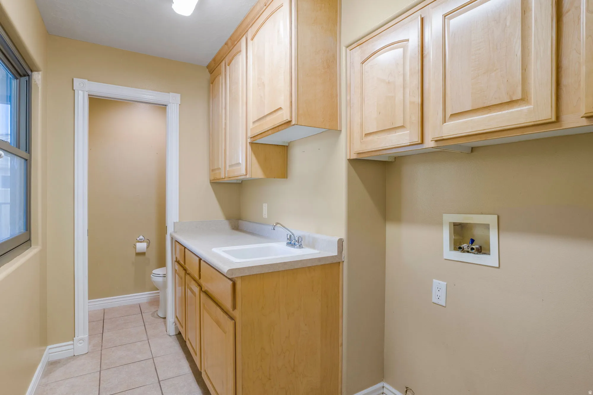 Light wood-finish cabinetry, integrated sink, tiled flooring, and a large window