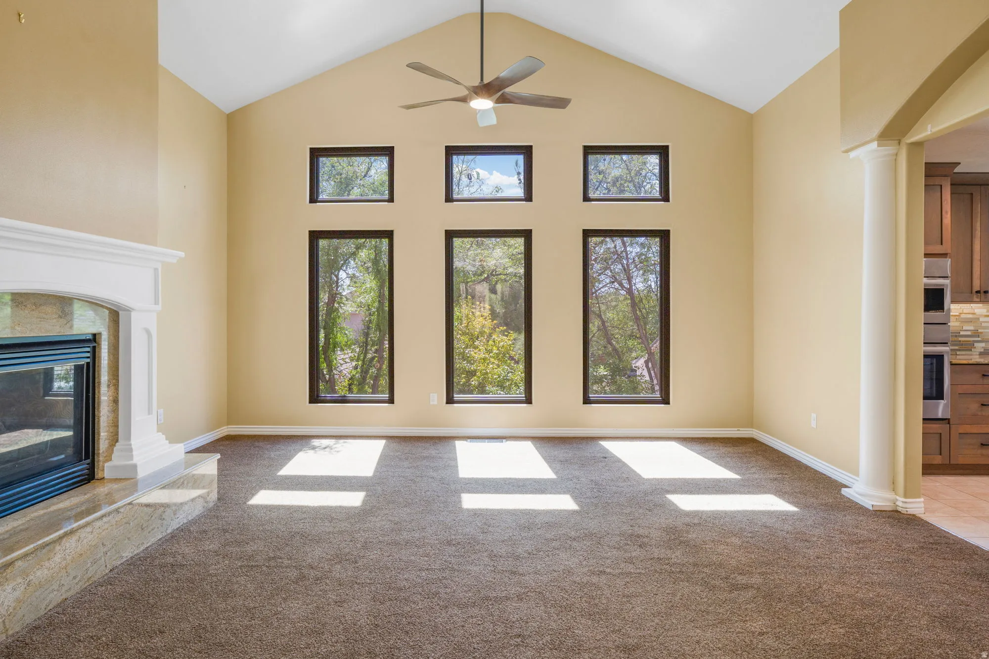Vaulted ceiling with a ceiling fan, multiple windows, fireplace with a mantel, and carpet flooring
