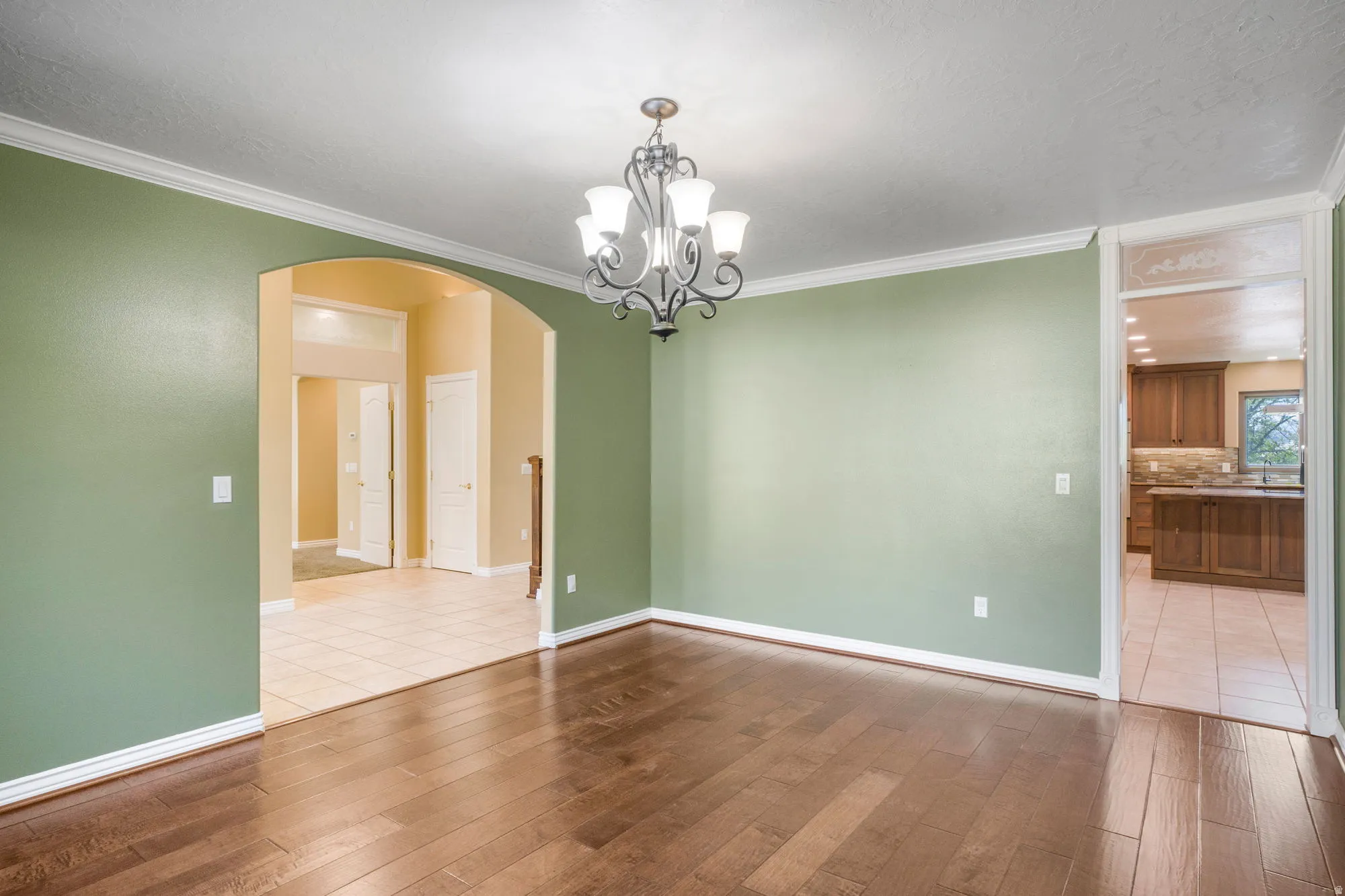Wood-finish flooring, crown molding, archway entry, and a chandelier fixture