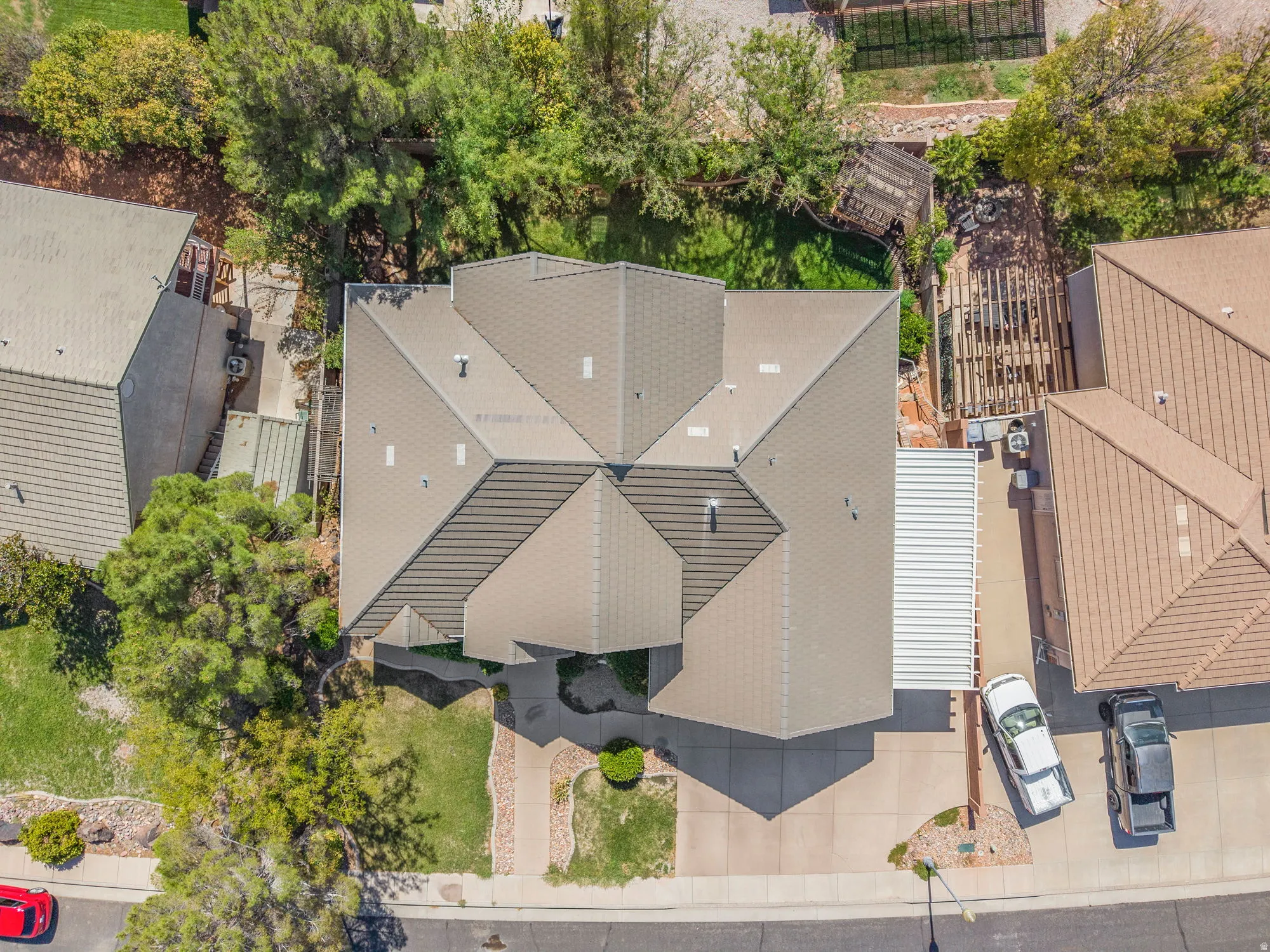 Pitched roofline, front yard with mature trees, established landscaping, concrete driveway, and covered parking structure