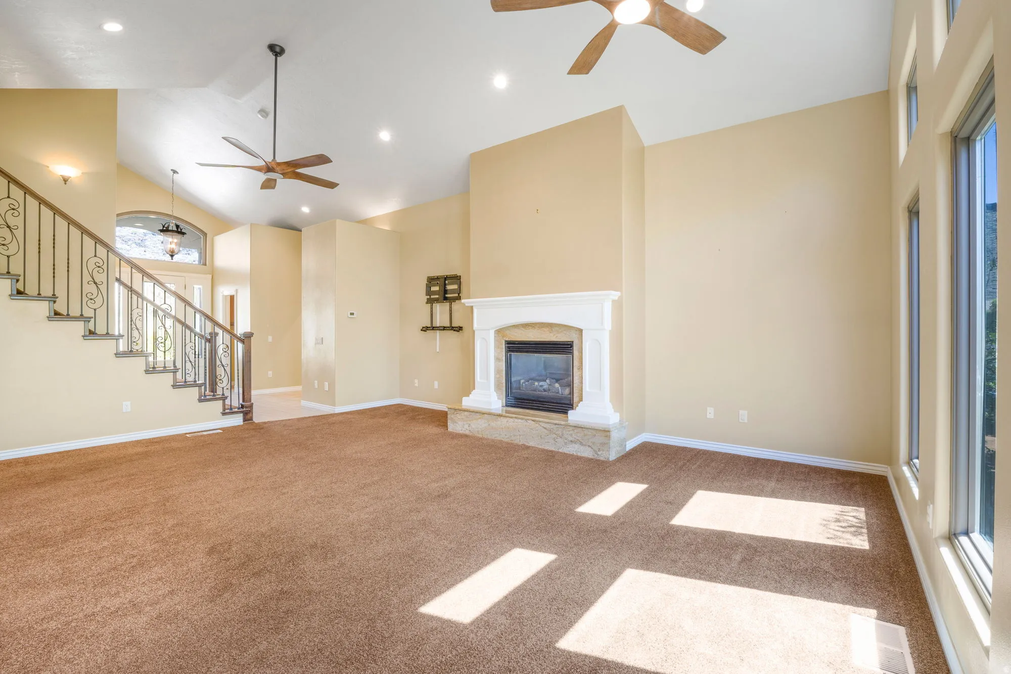 Vaulted ceiling with recessed lighting and ceiling fans, wrought iron stair railing, and a fireplace with a stone hearth