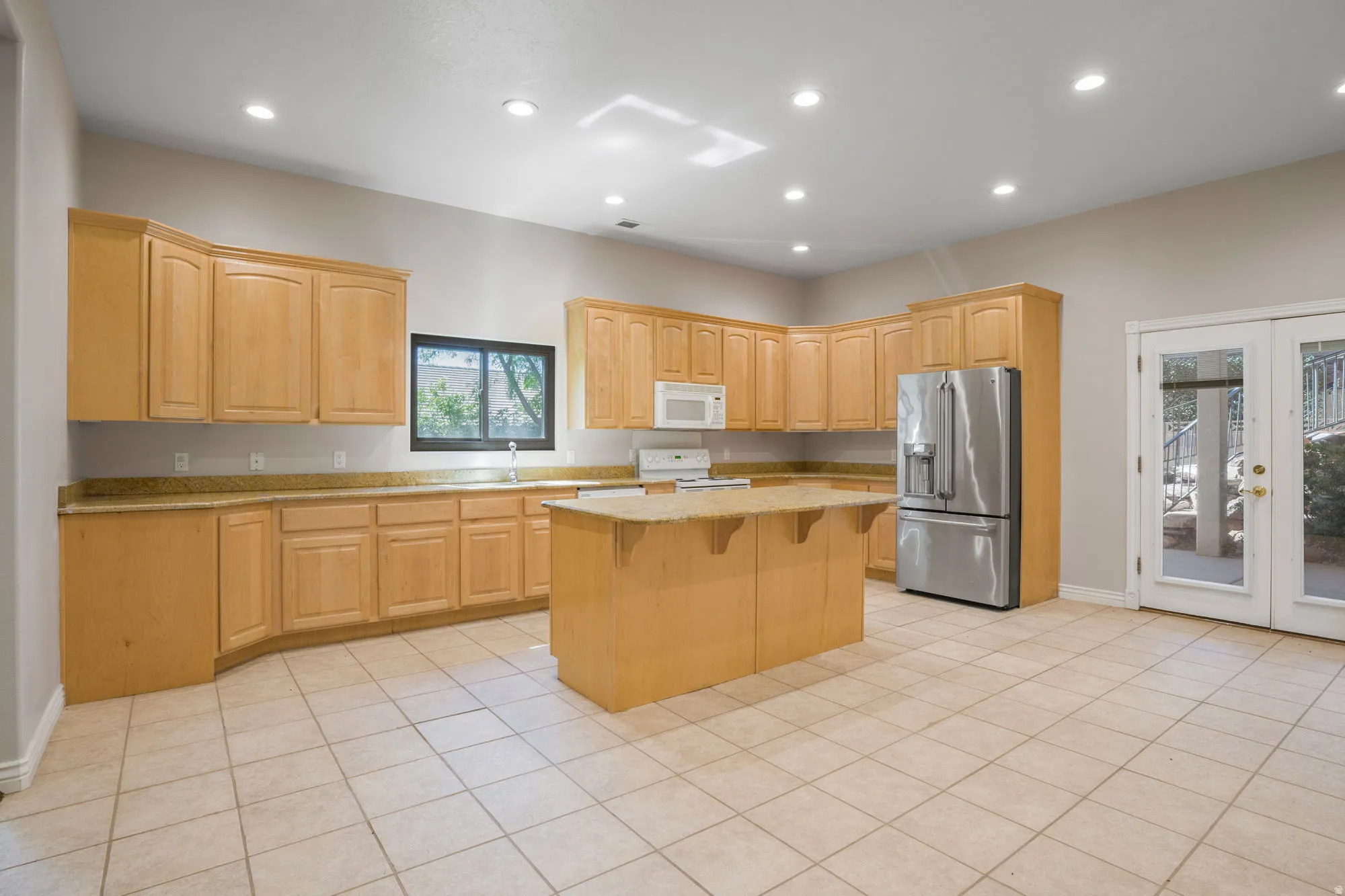 Kitchen featuring light wood cabinetry, stone countertops, a central island, stainless steel appliances, and French doors
