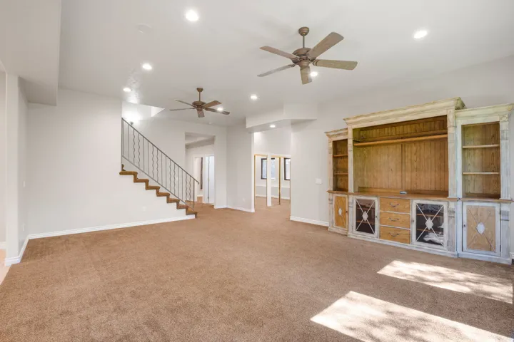 Carpeted living space featuring recessed lighting, two ceiling fans, and a built-in entertainment center