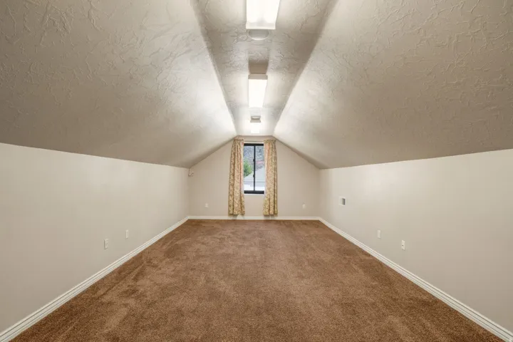 Spacious room with sloped ceilings, brown carpet, textured walls, and a recessed window