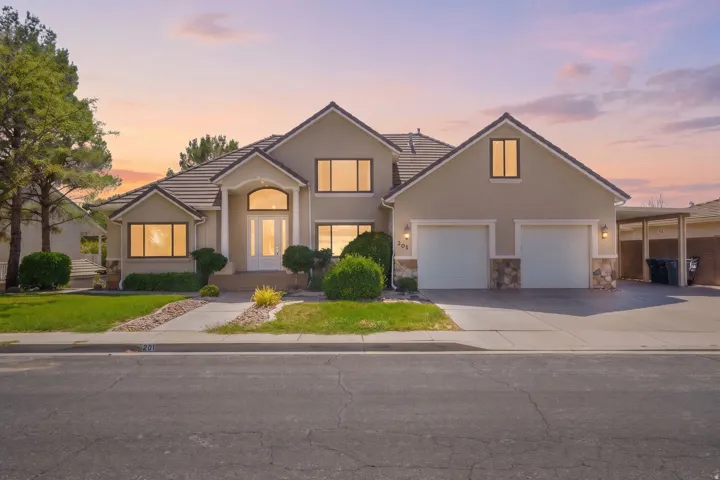 Stucco exterior with a tiled roof, arched entry, dual garage doors, stone accents, and an attached carport