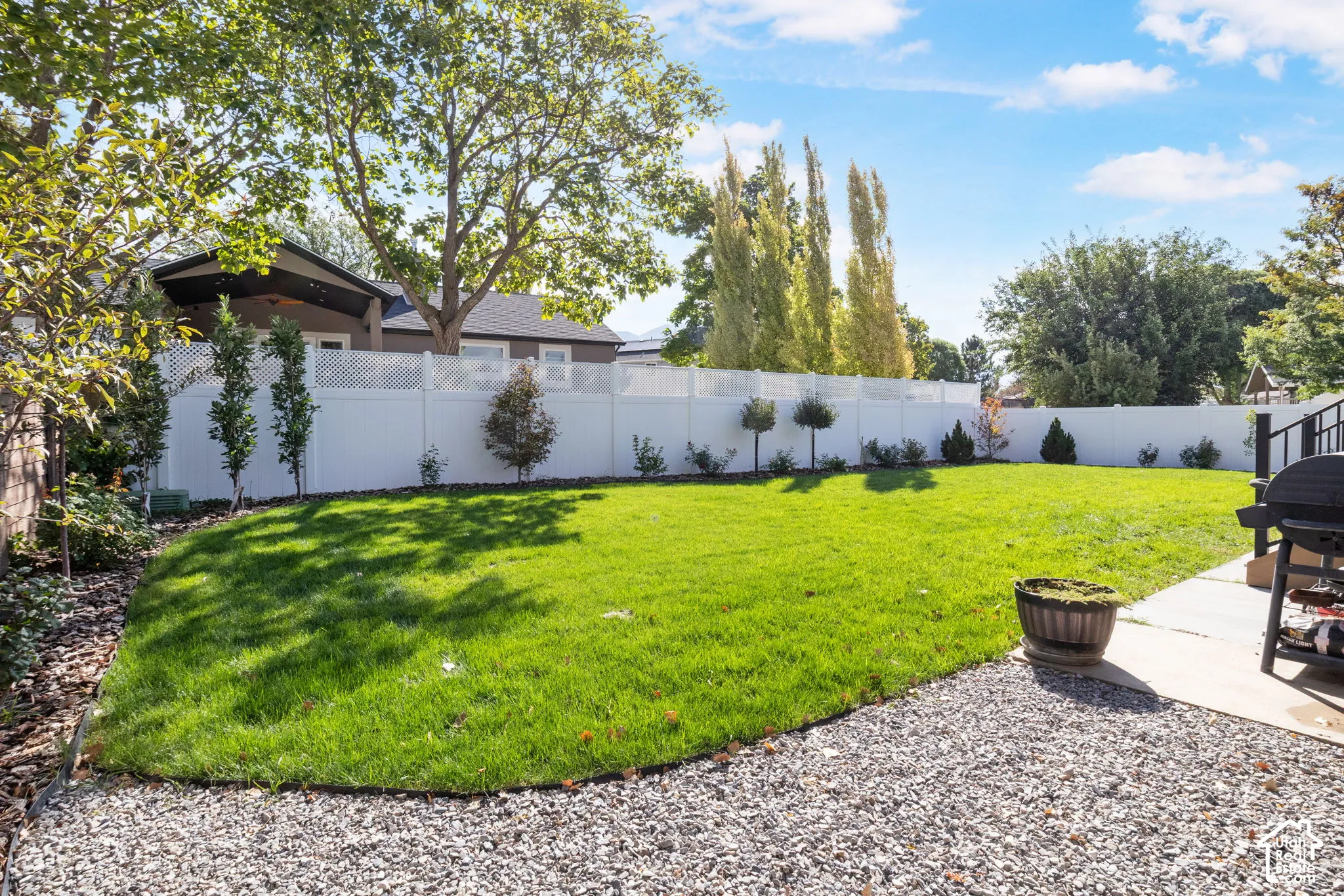 Expansive backyard featuring a manicured lawn, white privacy fencing with lattice detail, and mature landscaping