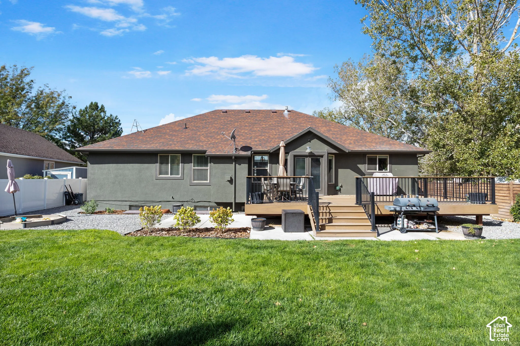 Expansive backyard featuring a manicured lawn, a multi-level wood deck with black metal railings, and a gravel hardscape area