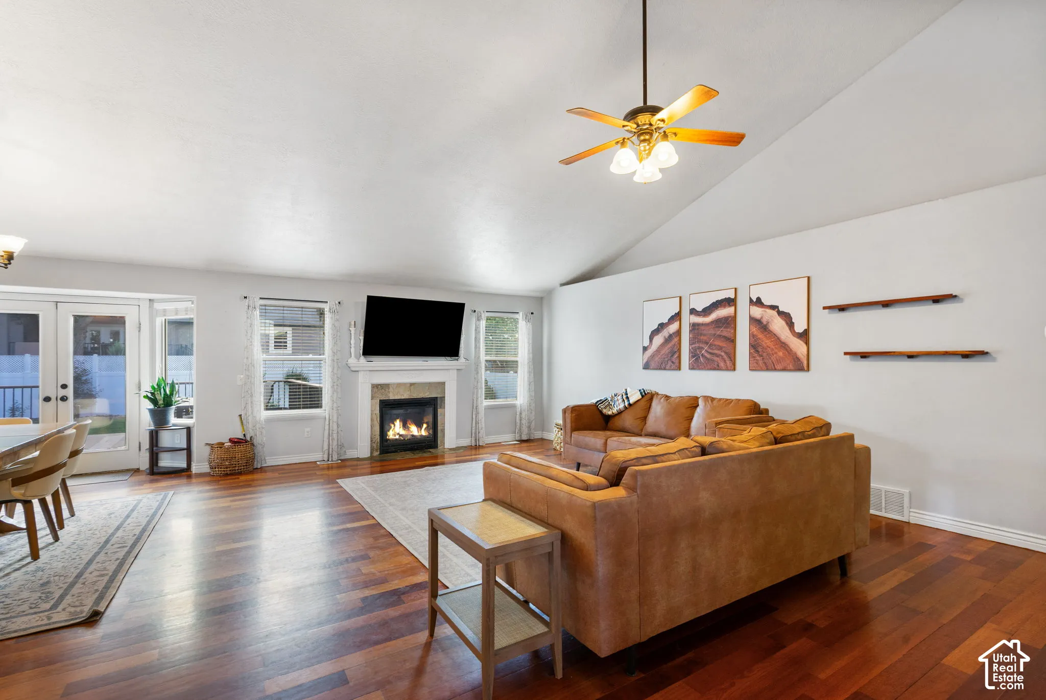 Wood-finish flooring throughout, vaulted ceiling, built-in fireplace with a mantel, double French doors, and a ceiling fan with integrated lighting