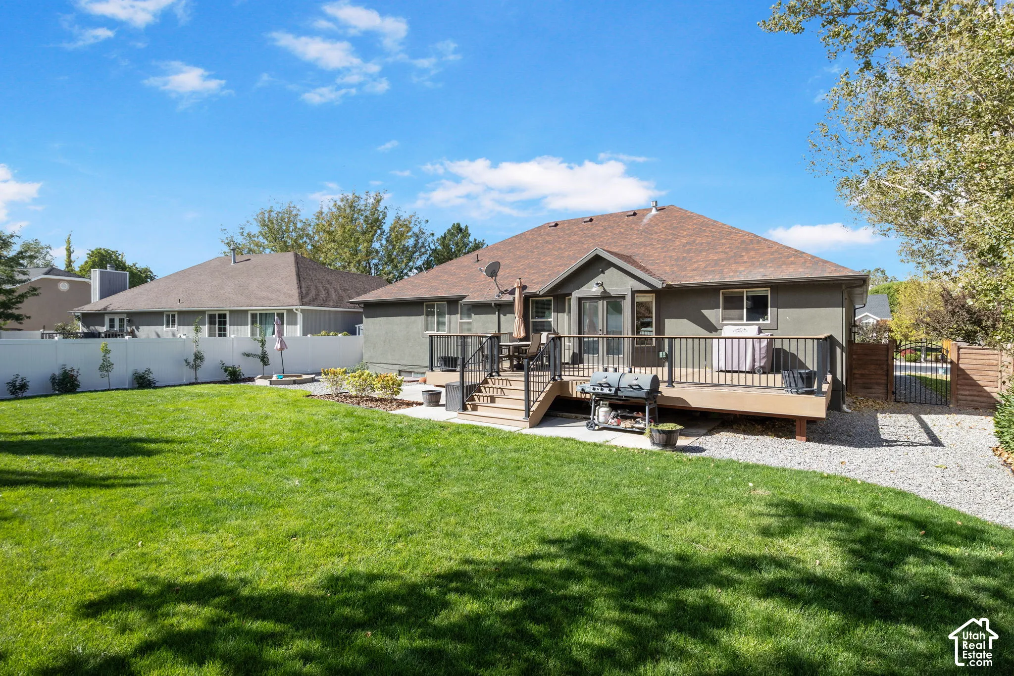 Expansive backyard featuring a large lawn area, a multi-level composite deck, a white vinyl fence, and a gravel pathway