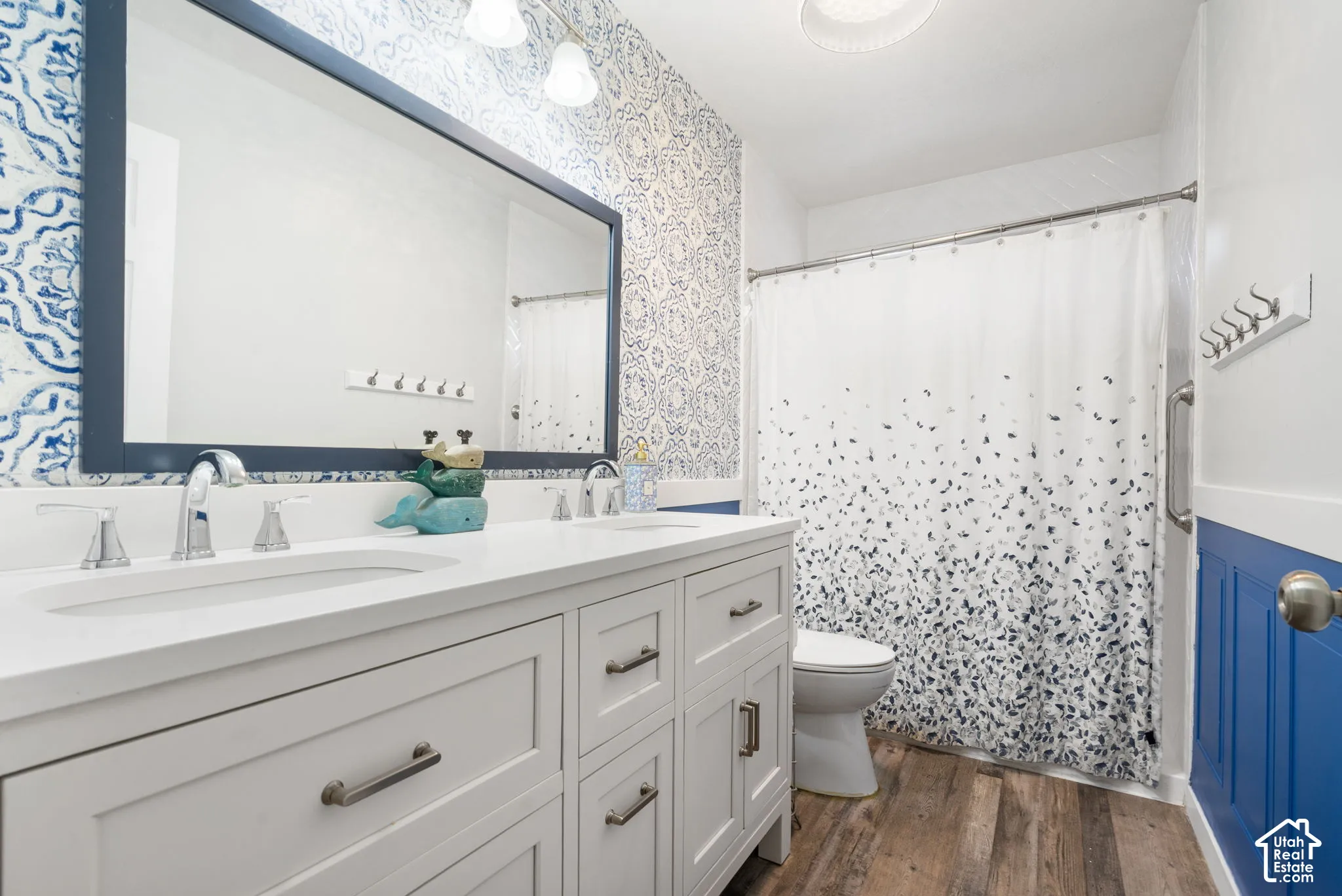 Dual vanity with integrated sinks, wood-finish flooring, framed mirror, and paneled accent wall