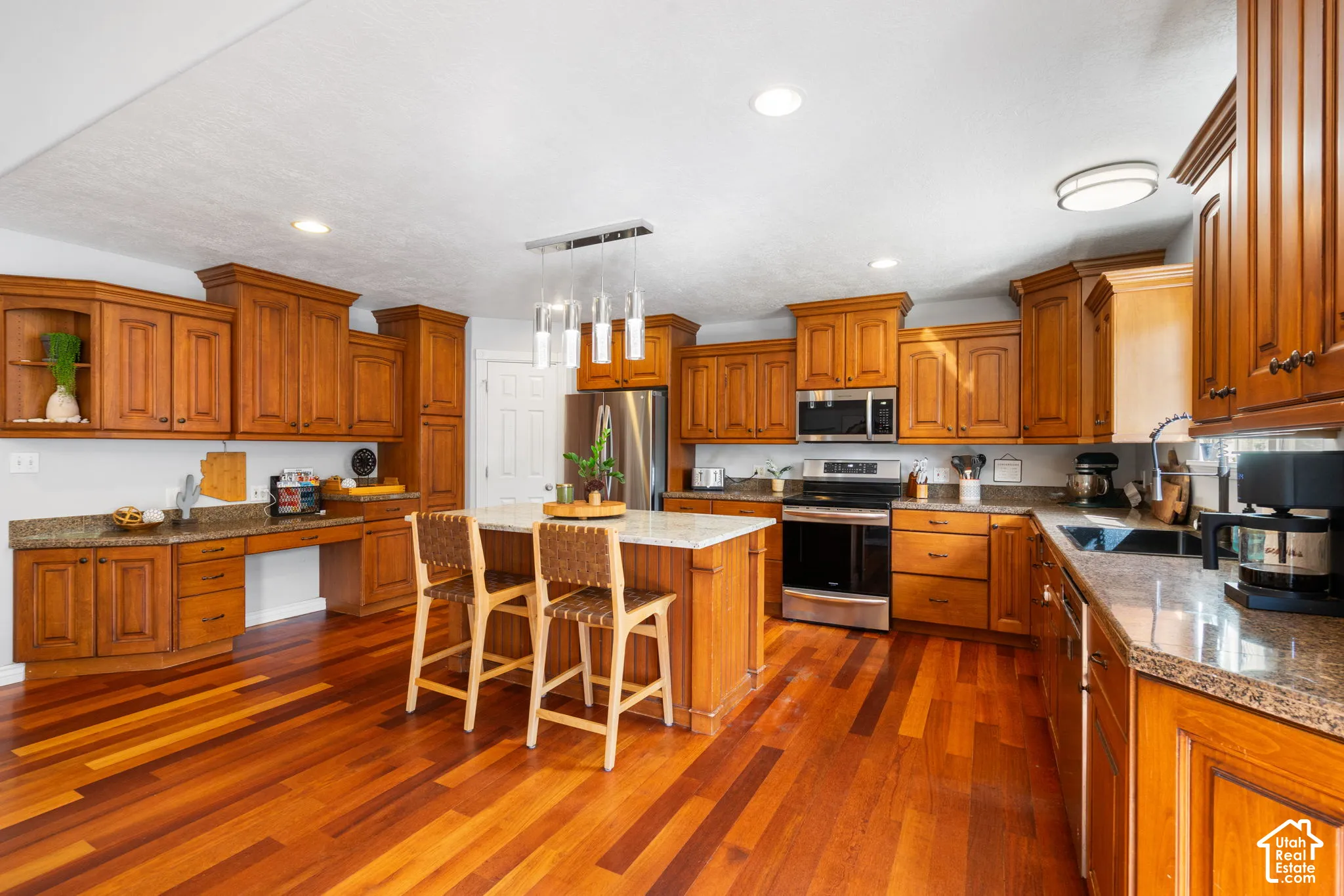 Wood-finish flooring throughout, extensive wood cabinetry, stainless steel appliances, granite-style countertops, and a central island with pendant lighting