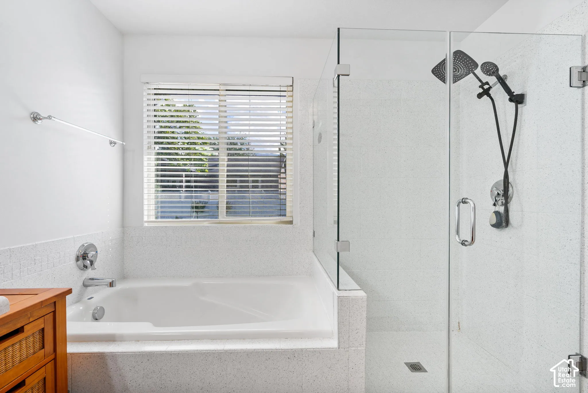 Built-in soaking tub with chrome fixtures, glass-enclosed shower with dual shower heads, and an exterior-facing window with horizontal blinds