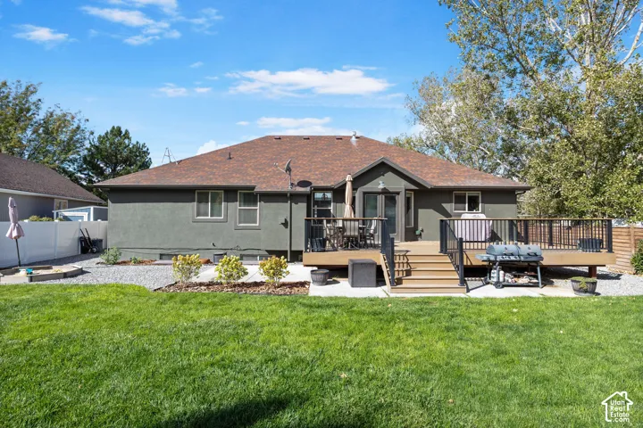 Expansive backyard featuring a manicured lawn, a multi-level wood deck with black metal railings, and a gravel hardscape area
