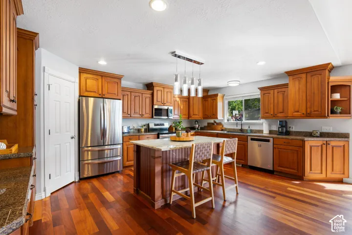 Wood-finish flooring, wood-finish cabinetry, stainless steel appliances, granite countertops, and a kitchen island with pendant lighting