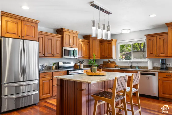 Kitchen featuring wood-finish cabinetry, stainless steel appliances, granite countertops, a center island, and wood-finish flooring