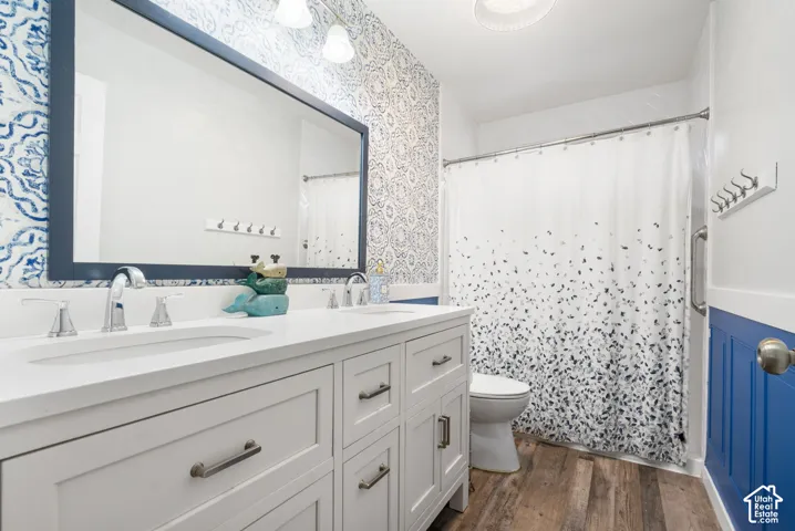 Dual vanity with integrated sinks, wood-finish flooring, framed mirror, and paneled accent wall