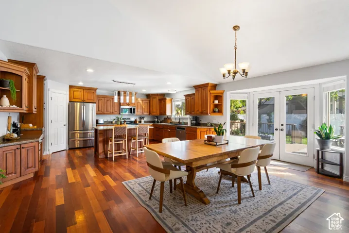 Open-concept kitchen and dining area featuring wood-finish flooring, wood cabinetry, stainless steel appliances, a kitchen island with seating, and French doors