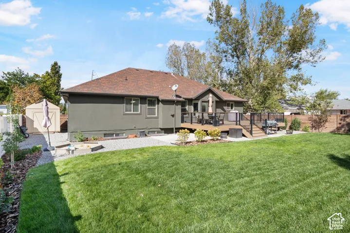 Expansive backyard featuring a manicured lawn, a multi-level wood deck, a storage shed, a gravel patio area, and mature trees
