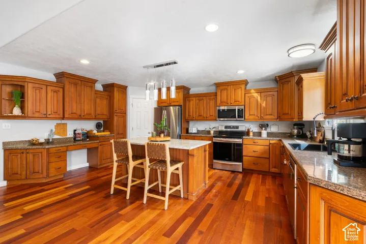 Wood-finish flooring throughout, extensive wood cabinetry, stainless steel appliances, granite-style countertops, and a central island with pendant lighting
