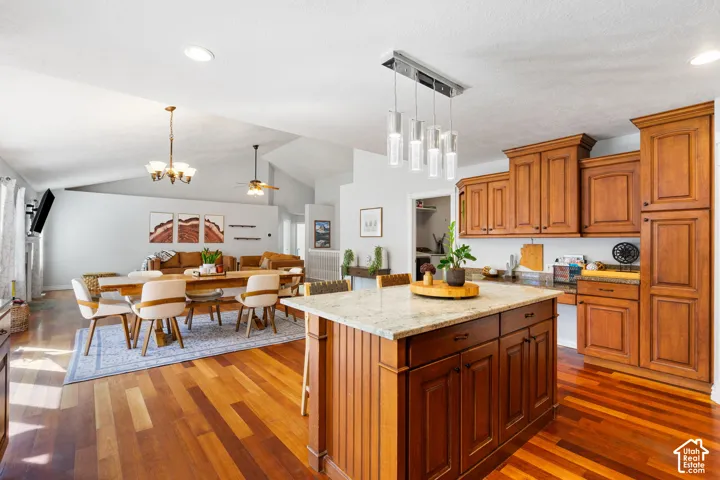 Vaulted ceiling with recessed lighting, wood-finish flooring, kitchen island with stone countertop, wood cabinetry, and a contemporary linear pendant light fixture