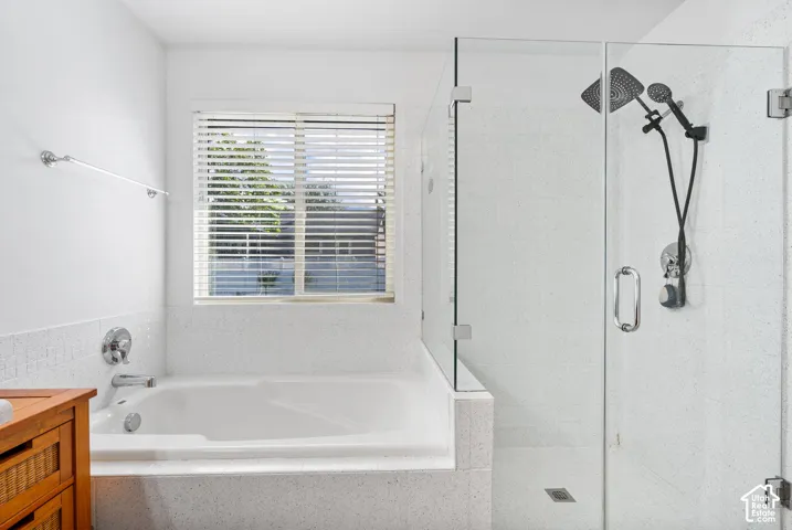 Built-in soaking tub with chrome fixtures, glass-enclosed shower with dual shower heads, and an exterior-facing window with horizontal blinds