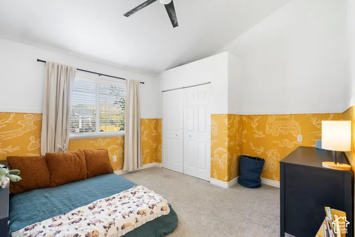 Vaulted ceiling with a ceiling fan, window with blinds, carpet flooring, and bi-fold closet doors